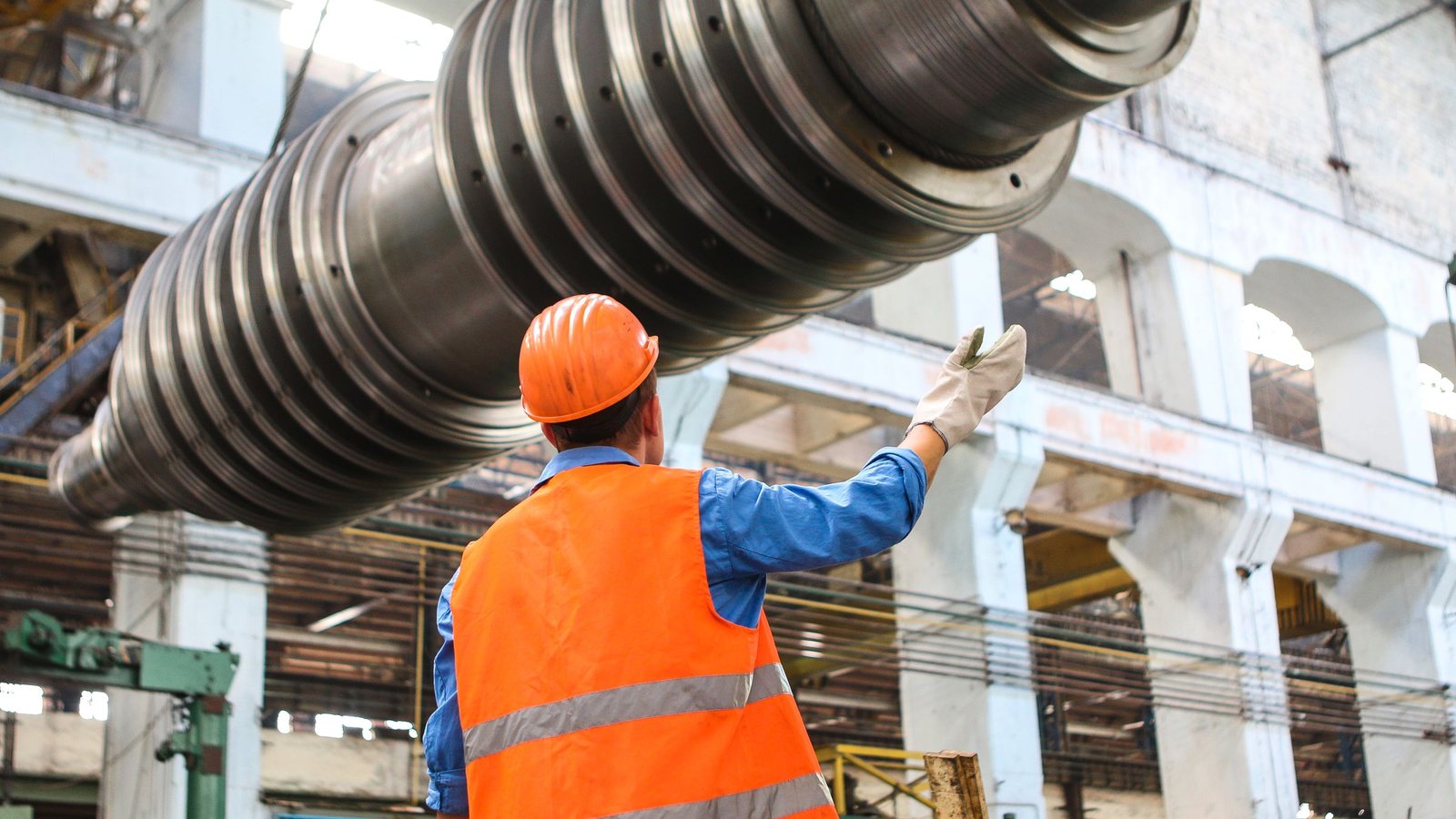 Worker in hard hat guiding a large steel roll inside a heavy industry plant