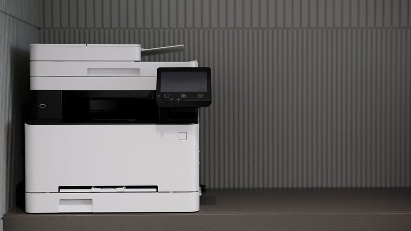 A modern multifunction printer and scanner on an office cabinet