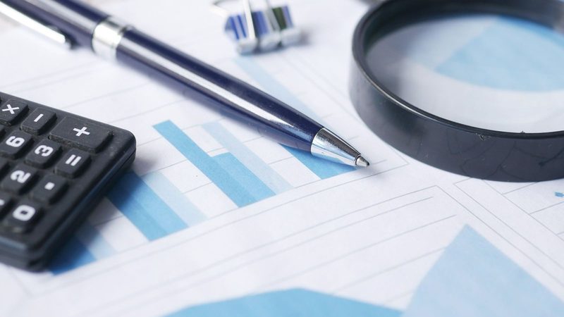 Calculator, pen and magnifying glass resting on printed financial charts