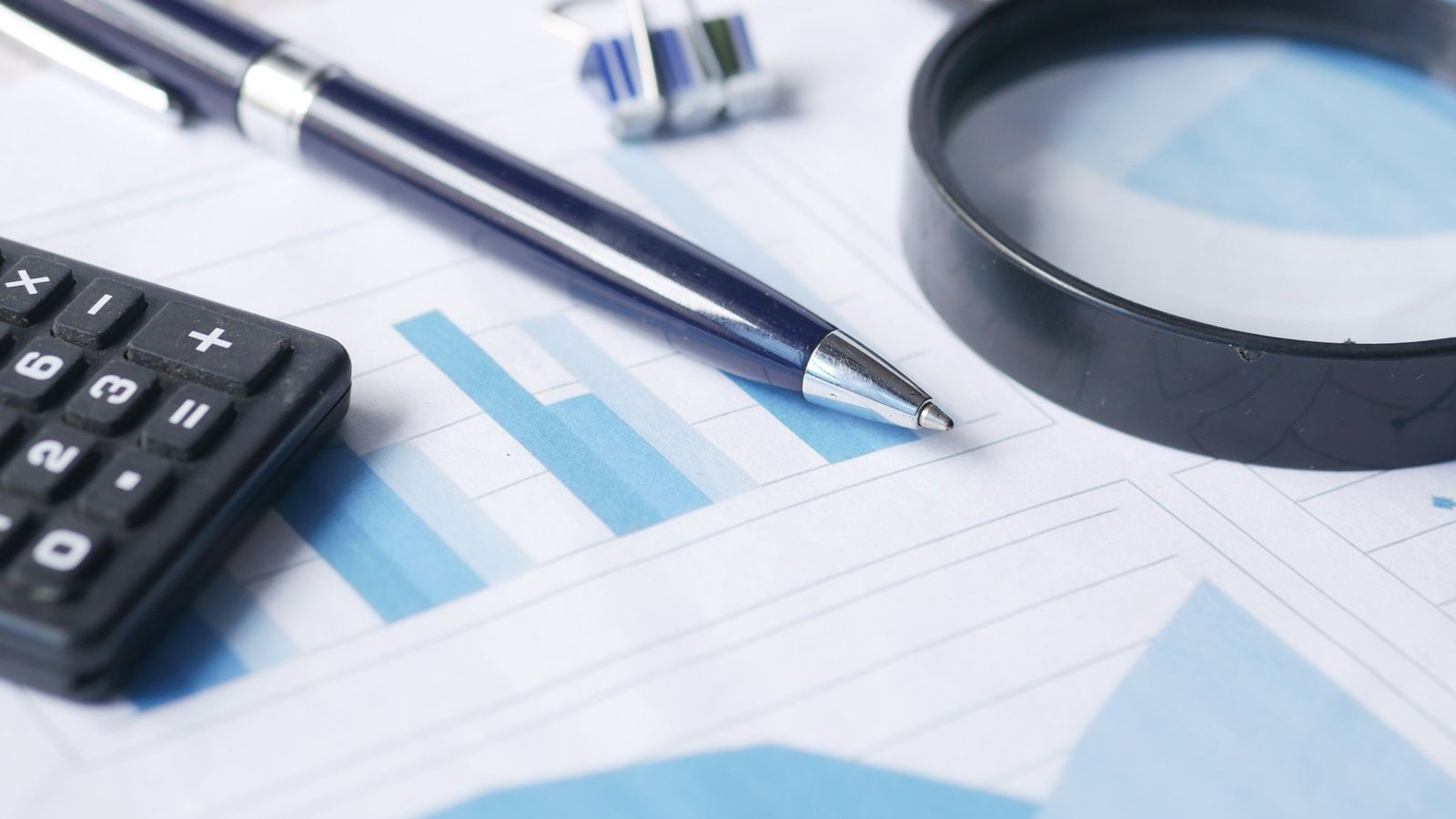 Calculator, pen and magnifying glass resting on printed financial charts