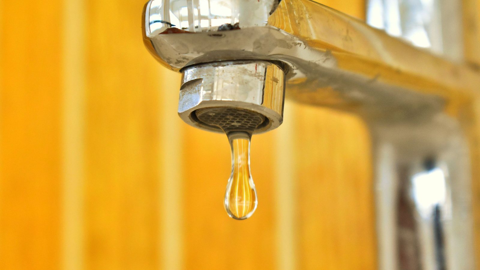 A single drop of water falling from a chrome tap